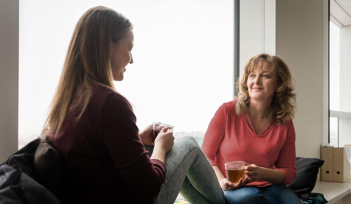 Alt text: Madre hablando con su hija mientras toman té en casa