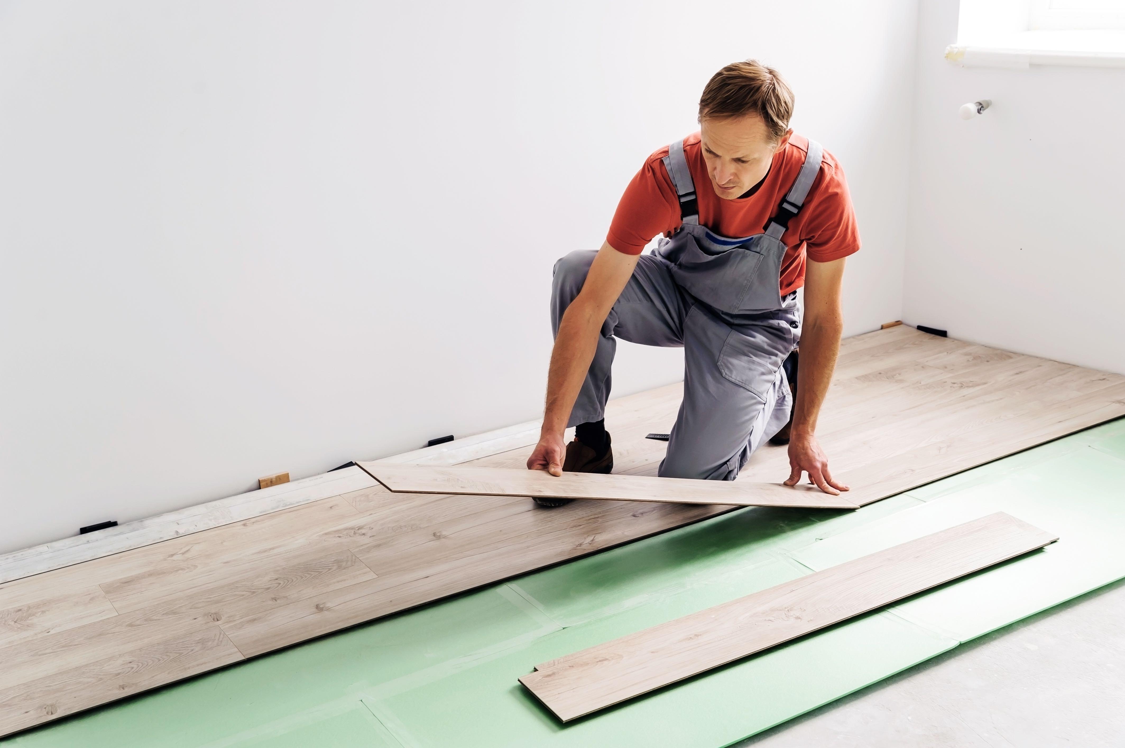 man in overalls laying down laminate flooring