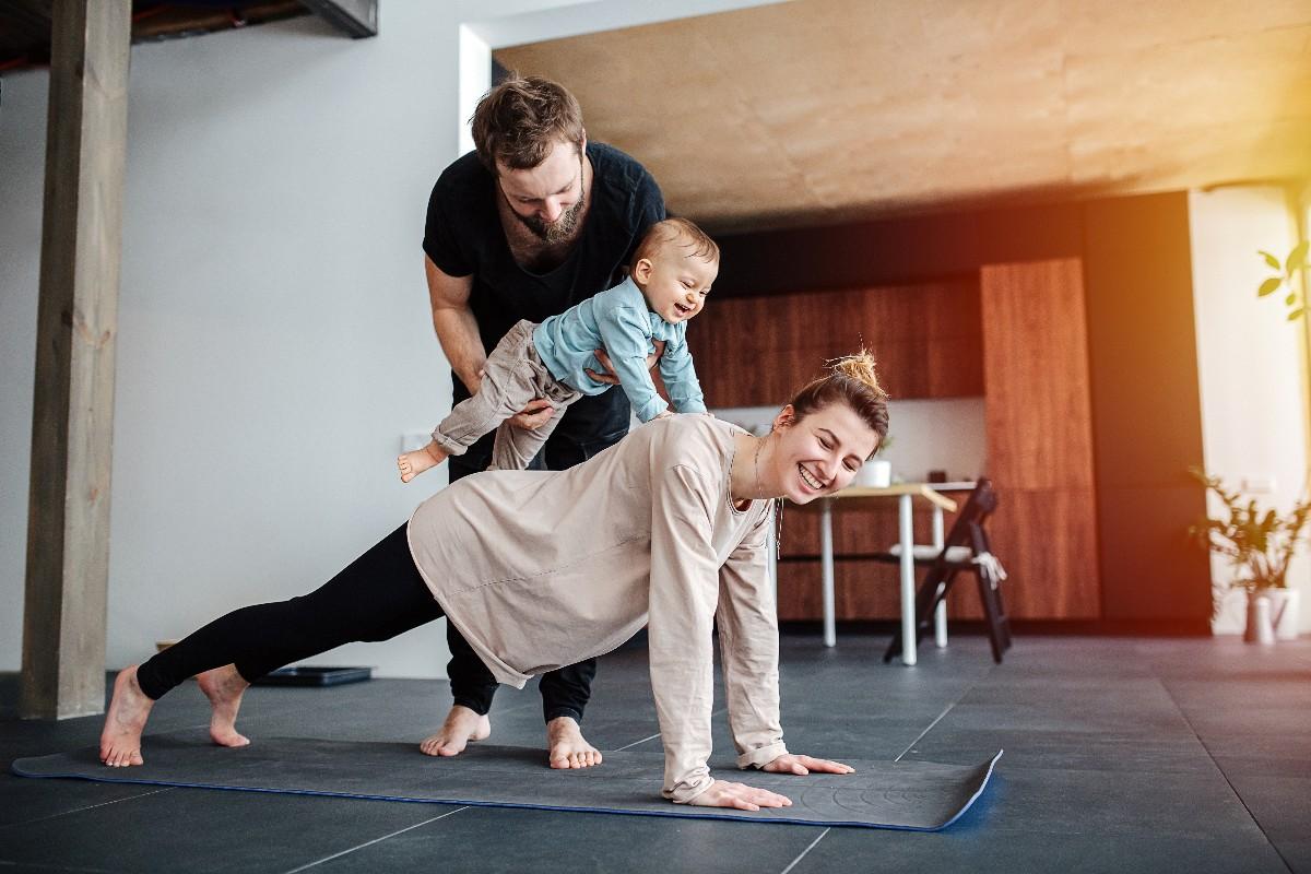 Family morning exercise. Mother doing plank, father holding baby on her back
