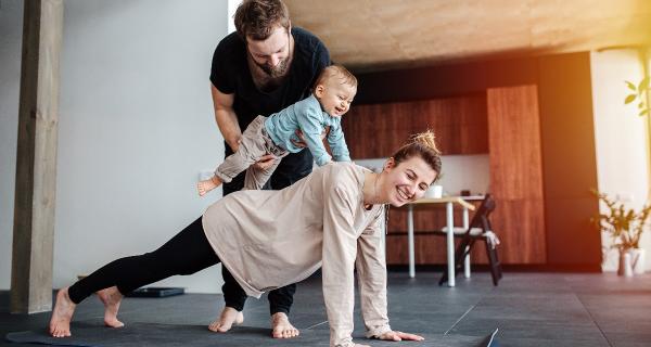 Family morning exercise. Mother doing plank, father holding baby on her back